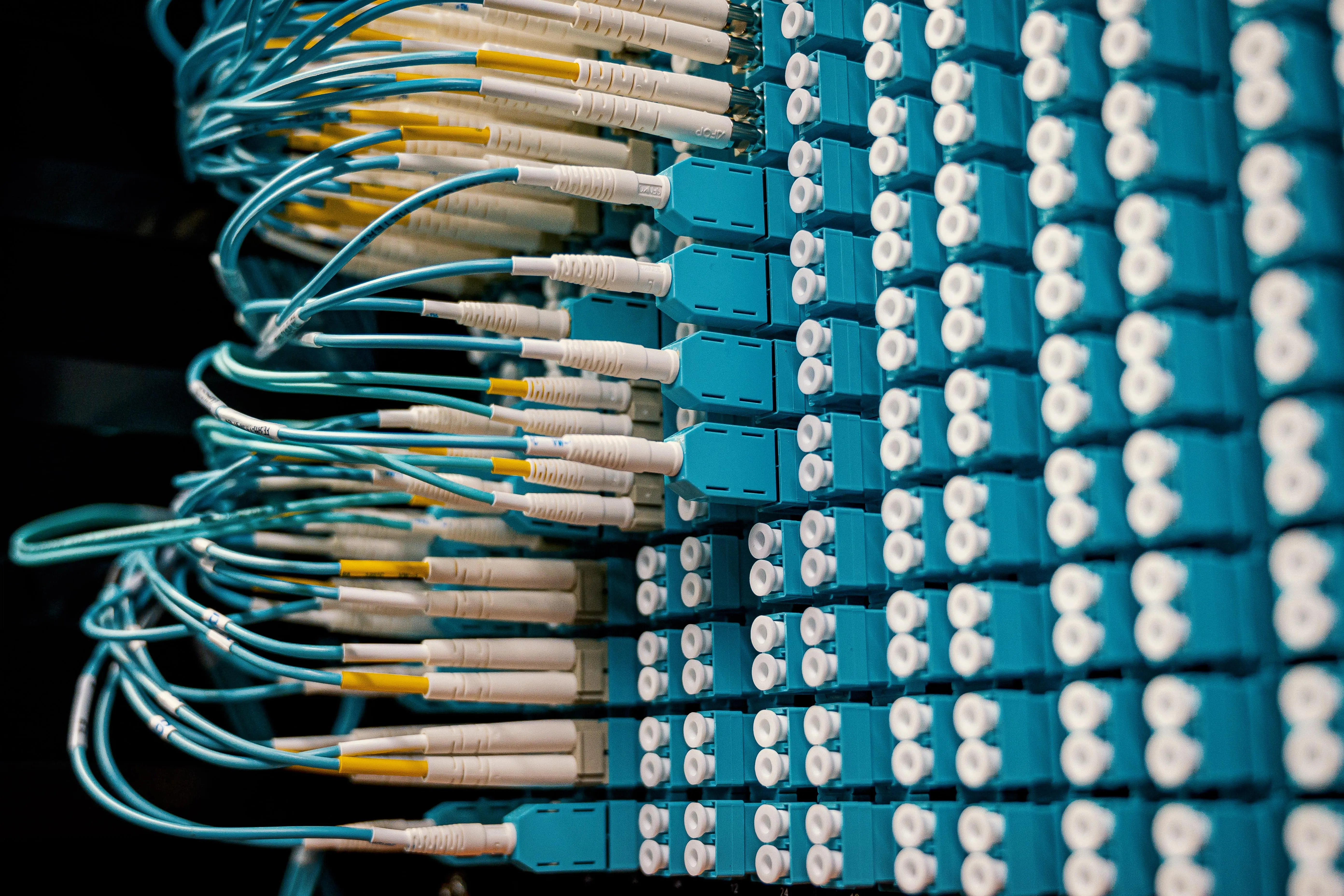 A dense fiber-optic patch panel of teal connectors, representing Simgen's connected, real-time device network